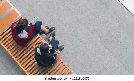 Top View Of Girls Group Use Smart Phone And Talk On Wood Bench