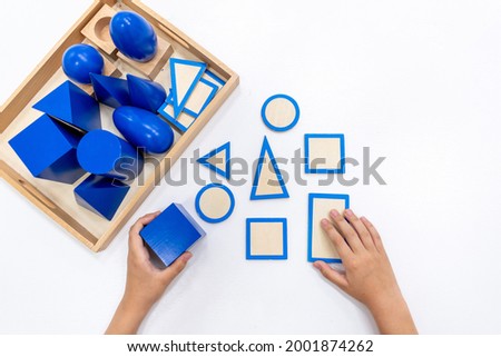 Top view of girls hand is playing and sorting a puzzle of colored wooden geometric shapes in montessori school. Concept of using a mathematical geometry learning resources for children education.