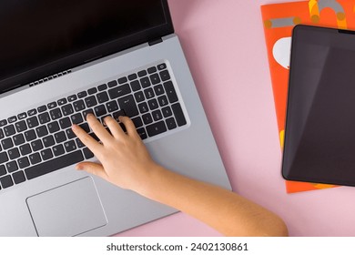 Top view of girl's hands typing on laptop keyboard with tablet on pink background - Powered by Shutterstock