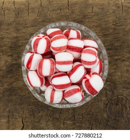 Top view of a glass bowl filled with peppermint balls on an old brown wood board.