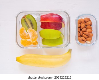 Top View, Glass Container Lunch Box Of Fresh Fruit With Apple, Kiwi, Banana, Orange And Almond On White Wooden Background. Take Away Food, With Blank Space For Text, Healthy Eating Concepts.
