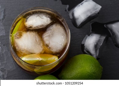 Top View Of A Glass Of Cuba Libre Cocktail With Rum, Coke, Lemon And Lime Slices And Some Ice Cubes. Focus On The Ice In The Glass