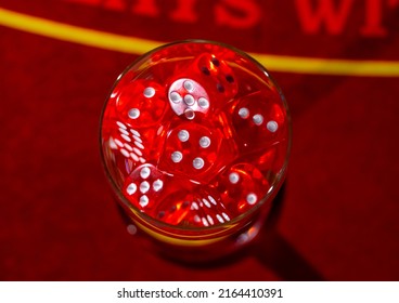 Top View Of A Glass Filled With Red Dice. A Set Of Dice For Craps, Poker, Roulette On A Red Gaming Table In A Casino. Close Up. Background Of Gambling, Entertainment, Leisure.