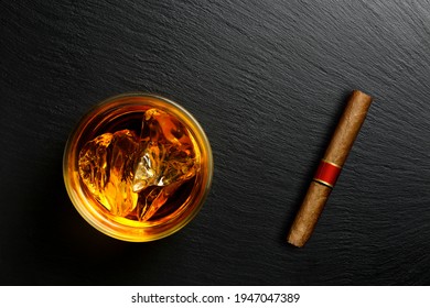 top view of glass of whiskey and cigar on black stone surface with copy space