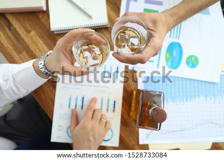 Top view of glassful with alcoholic beverage with ice-cubes in male hands. Colleague sitting at table in office celebrating signing profitable contract. Biz negotiations concept. Blurred background
