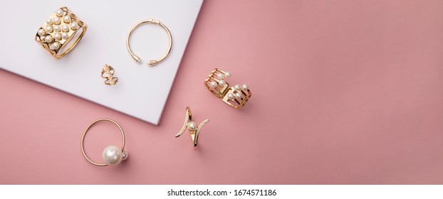 Vista superior de brazaletes dorados y perlas sobre fondo rosa y blanco con espacio para copiar
