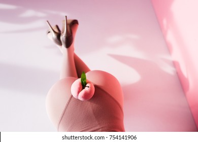 Top View Of Gorgeous Girl On Bodysuit Posing With Peach On Buttocks In Studio  