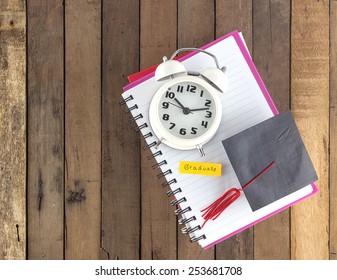 Top View Of Graduation Cap And Clock  On Notebook