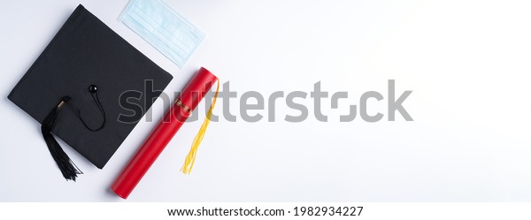 Top view of\
graduation square academic cap with degree diploma and mask\
isolated on white table\
background.