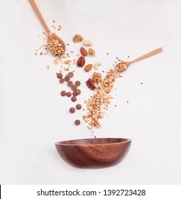 top view of granola ingredients in wooden spoons fall into a bowl. isolated in white background. Crunchy granola, muesli. Healthy dessert snack.