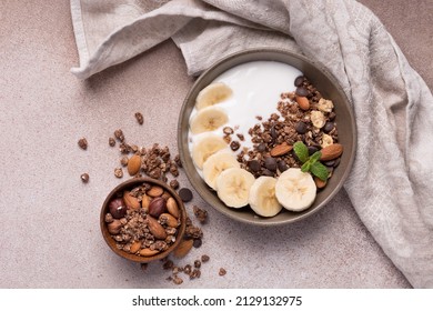 Top view of granola with yogurt, fresh banana, chocolate drops and almond nuts for healthy breakfast on brown concrete background - Powered by Shutterstock