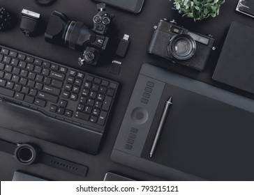 top view of graphic design work station, work space concept with retro camera, digital camera, memory card, smartphone, graphic tablet, and keyboard on black background