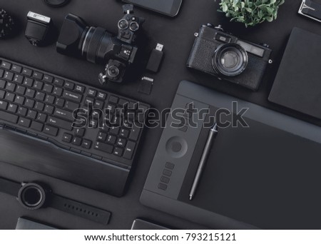 top view of graphic design work station, work space concept with retro camera, digital camera, memory card, smartphone, graphic tablet, and keyboard on black background