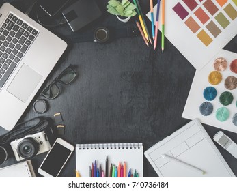 Top View Of Graphic Designer Work Space With Graphic Tablet, Smartphone, Sample Color Swatches, Thread Color Swatches, Laptop And Other Accessories On Black Wooden Background With Copy Space.