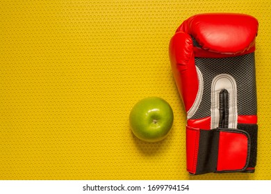 Top View Of A Green Apple And Red Boxing Glove On The Yellow Mat. Sport At Home, Fitness Practice 