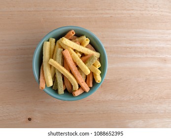 Top view of a green bowl filled veggie straws on a wood table.