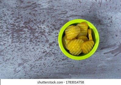 Top View Of A Green Bowl Filled With Hamburger Dill Pickle Slices Offset On A Gray Tabletop Illuminated With Natural Lighting.