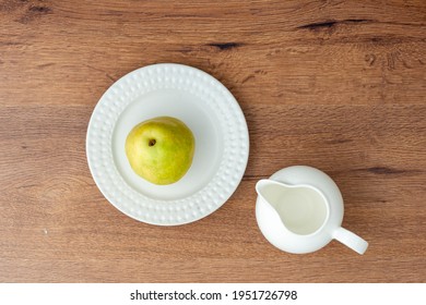 Top View Of Green Pear On A White Ceramic Plate And Empty Milk Jug On Wooden Table