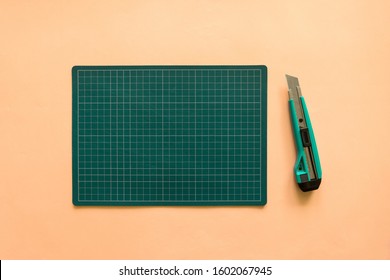 Top view of green rubber cutting mat with green cutter over pale orange color paper background. Background with copy space. - Powered by Shutterstock