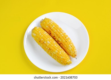 Top View Of Grilled Bbq Corn Cob On White Plate Isolated On Yellow Background With Burn Juicy Golden Texture. Healthy Food Summer Fun Background And Design Element. Copy Space.