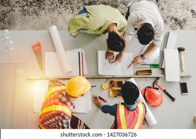 top view of group of engineer, technician and architect planning about building plan with blueprint and construction tools on the conference table at construction site, contractor and teamwork concept