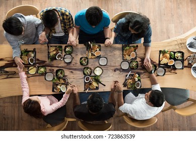 Top View Group Of Friends Or Family Holding Hands And Praying Over Food At Dinner Table  Together In The Restaurant.