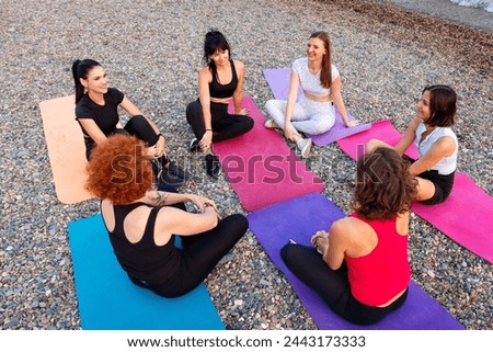 Top view of group of happy young-adult multi-racial women are sitting on sports mats on wild beach and talking to each other. Concept of female circle of communication and support.