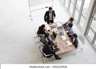 Top View Of Group Of Multiethnic Busy People Working In An Office, Aerial View With Businessman And Businesswoman Sitting Around A Conference Table With Blank Copy Space, Business Meeting Concept