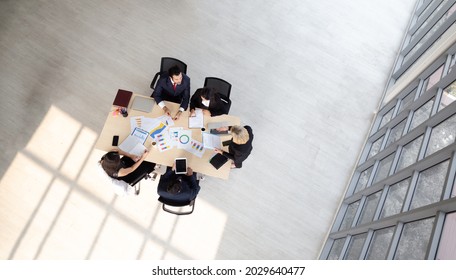 Top View Of Group Of Multiethnic Busy People Working In An Office, Aerial View With Businessman And Businesswoman Sitting Around A Conference Table, Business Meeting Concept