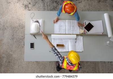 Top view of group of professional engineering team wearing safety helmet is meeting and pointing finger up,Architects planning construction work and create with blueprint at construction site