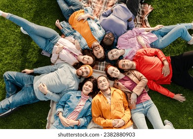 Top view group of smiling attractive multicultural friends wearing colorful clothing meeting, relaxing, chilling lying on green grass in park. Diversity, friendship, vacation, travel concept  - Powered by Shutterstock