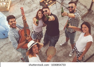 Top View Of A Group Of Young Friends Having Fun At A Rooftop Party, Playing The Guitar, Singing And Enjoying Hot Summer Days. Focus On The Couple In The Middle