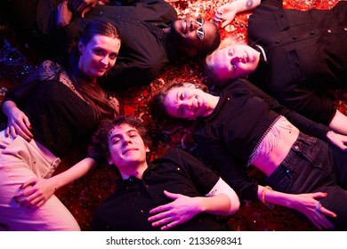 Top View At Group Of Young People Lying On Floor At Party With Confetti Falling, All Looking At Camera