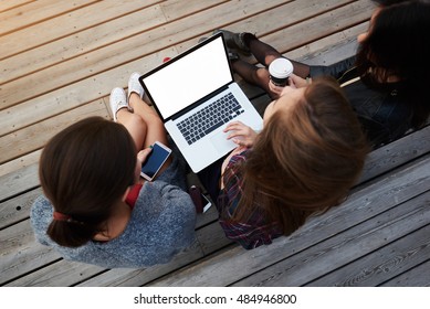 Top View Of Group Of Young Students Are Watching Movie On Laptop Computer, While Are Sitting On Campus During Lectures Break. Three Women Using Net-book, While Are Resting Outdoors After Walking Tour