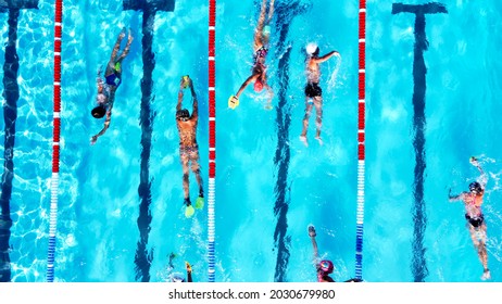 Top view of group of young swimmers training in swimming pool with marked lanes outdoor. Many sportive people and kids swim in Open Water Swimming pool with clean blue water. Summer sports camp