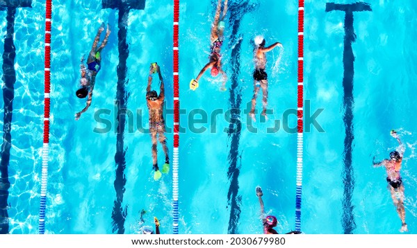 Top view of group of young swimmers training in\
swimming pool with marked lanes outdoor. Many sportive people and\
kids swim in Open Water Swimming pool with clean blue water. Summer\
sports camp