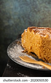 Top View Of Half Yogurt Sponge Cake On Dark Plate With Sugar And Wooden Fork, On Wooden Table And Gray Background, In Vertical, With Copy Space