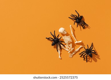 Top view of halloween composition with black spiders and broken plastic skeleton on orange background. Creative and minimal halloween concept, copy space - Powered by Shutterstock