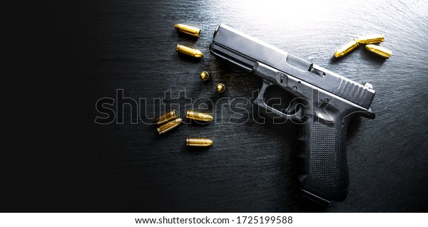 Top view of hand\
gun on black background with bullets around. 9mm pistol with\
ammunition on dark table.