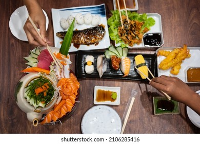 Top view hand holding chopsticks to hold fresh salmon sliced for sushi menu.A set of sushi on a wooden table in a Japanese restaurant.Party of friends or family eating sushi using bamboo sticks.