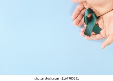 Top View Of Hand Holding Color Teal Awareness Ribbon. PCOS, Sexual Assault And Ovarian Cancer Care And Prevention Concept.