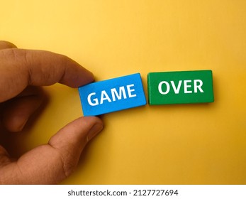 Top view hand holding colored block with text GAME OVER on a yellow background.