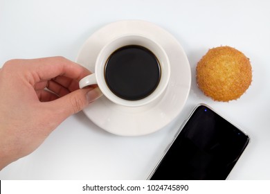 Top view, Hand holding of a espresso coffee in white cup with brownie muffin cakes and smartphone isolated on white background, Coffee break in concept in soft tone vintage background.