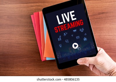 Top View Of Hand Holding Tablet With Live Steaming Word With Icon Over Color Notebook On Wooden Table Top,Digital Business Concept.