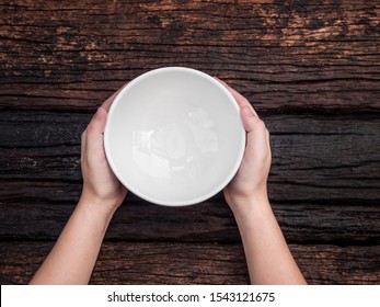 Top view hand holding white bowl on wood background
