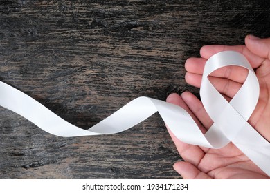 Top View Of Hand Holding White Ribbon On Dark Wood Background. Lung Cancer Awareness Concept.	