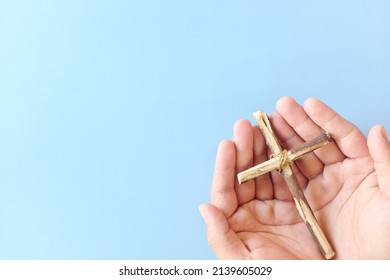 Top View Of Hand Holding Wooden Cross Crucifix With Copy Space In Blue Background. Catholicism, Christianity, Thanksgiving, Catholic And Christian Faith Concept.