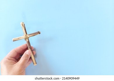 Top View Of Hand Holding Wooden Cross Crucifix With Copy Space In Blue Background. Catholicism, Christianity, Thanksgiving, Catholic And Christian Faith Concept.