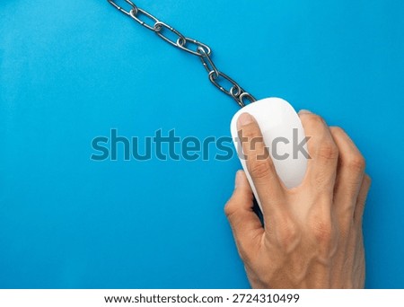 Top view of a hand on a computer mouse chained to a desk. Conceptual image for internet addiction, remote work burnout, digital slavery, office stress, and the need for a healthy digital detox.