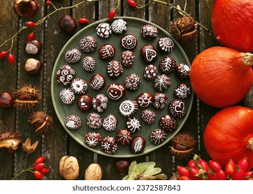 Top view of hand painted chestnuts with different funny motifs in a pate on the garen table with pumpkins and nuts. DIY autumn idea for children. 